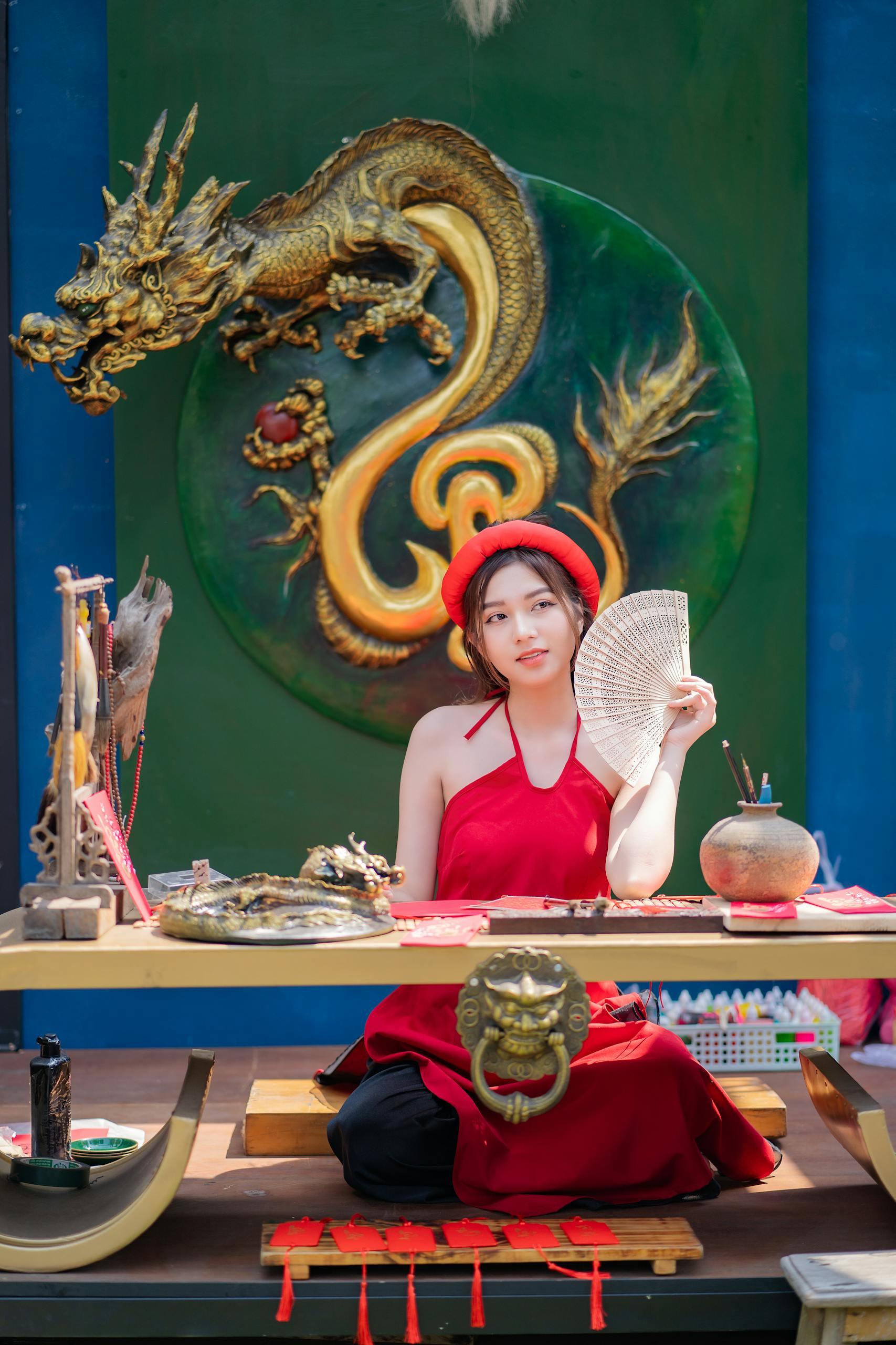 A woman in traditional attire sits at a decorated table in an Asian-themed restaurant with dragon art.