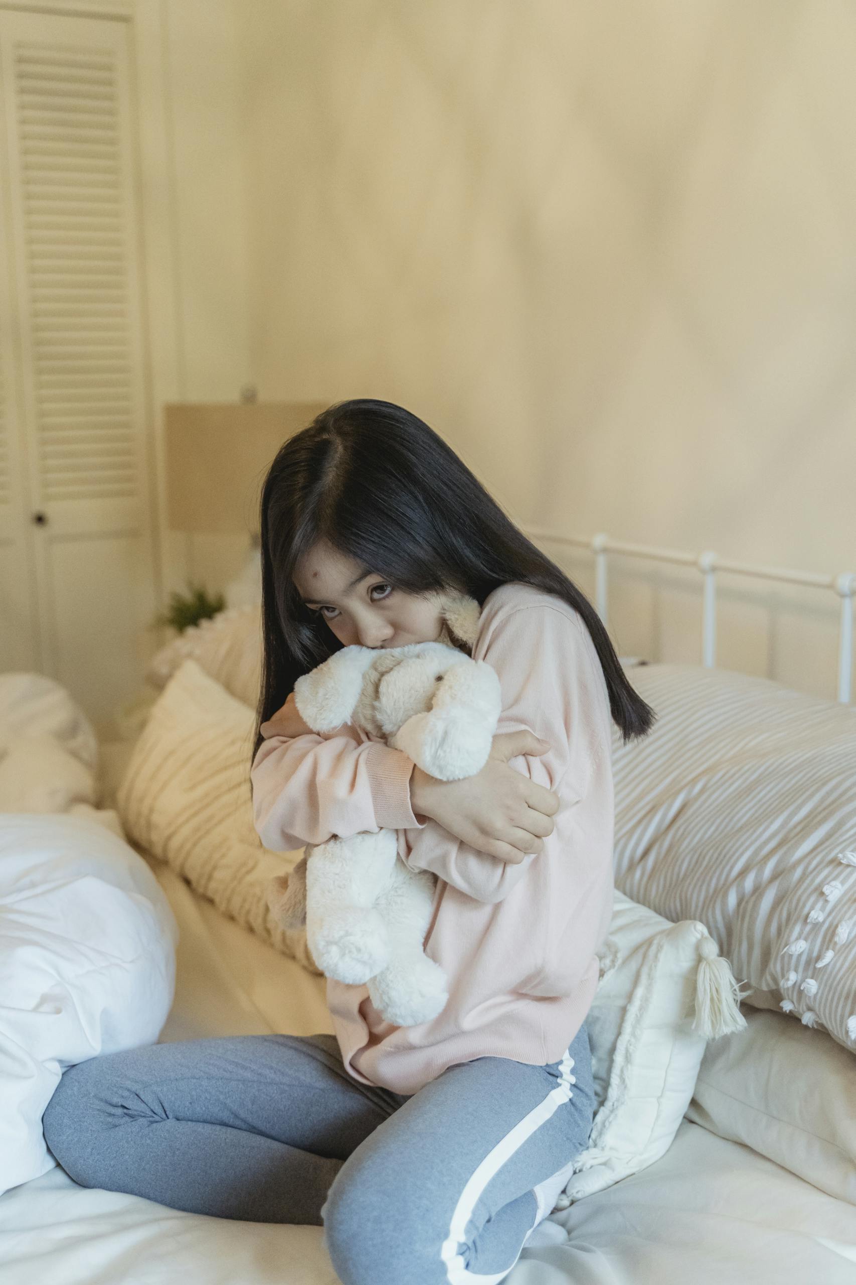 A young girl in a bedroom hugging a plush toy, creating a cozy and warm atmosphere.